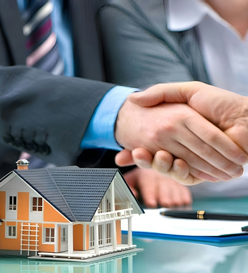 Two people shaking hands over a model house, representing a trusted real estate partnership